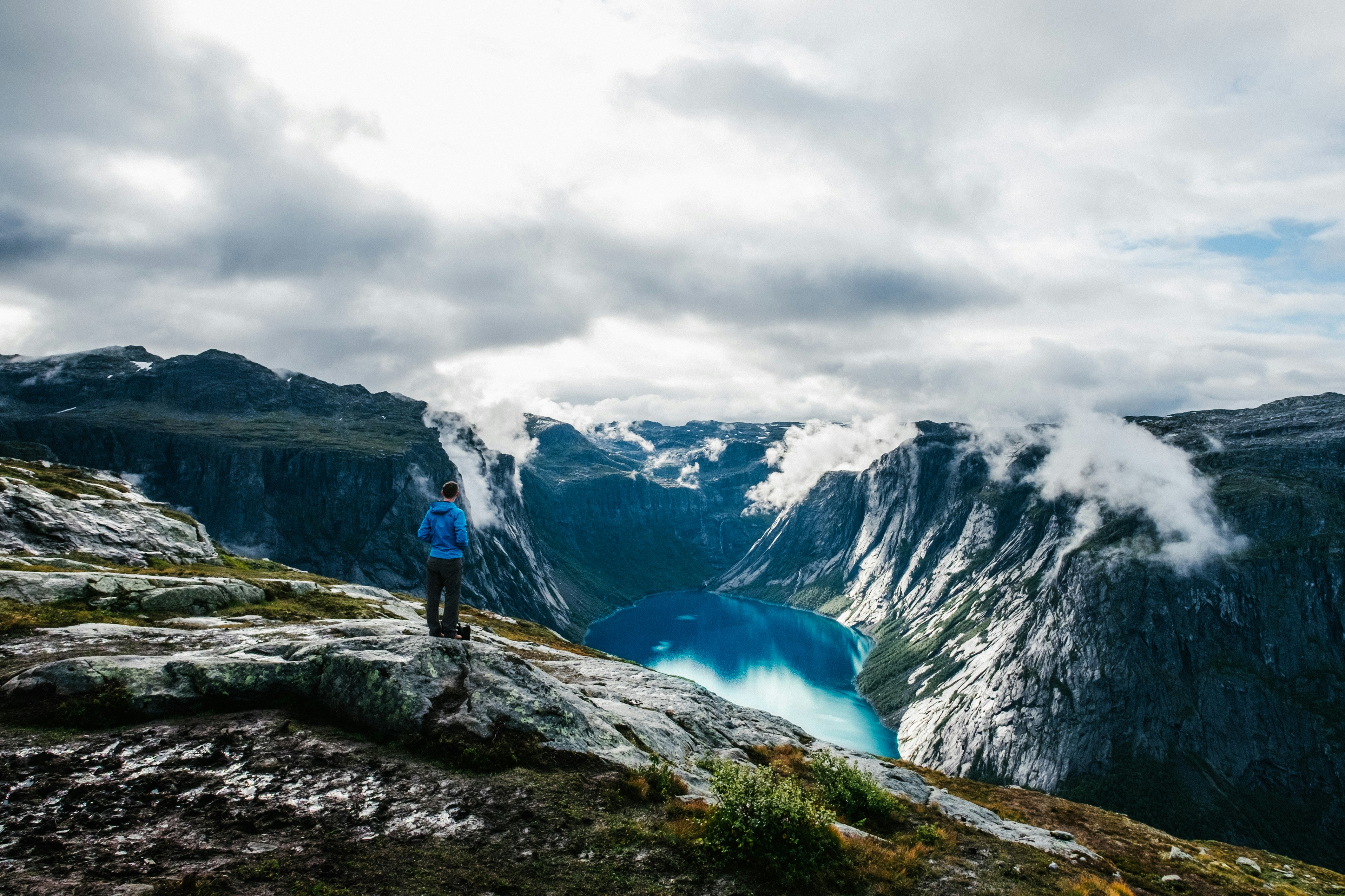 man wearing blue jacket standing on hill facing another hill